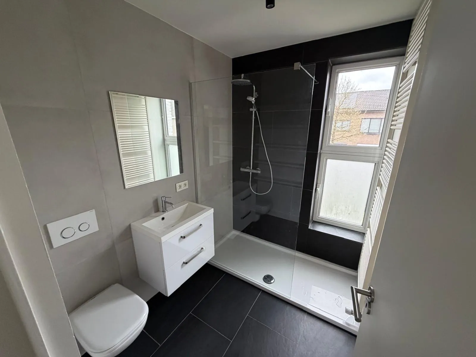 Afgewerkte badkamer met zwart betegelde doucheruimte, hangtoilet en handdoekradiator, gerenoveerd door HS Concept in Aalst