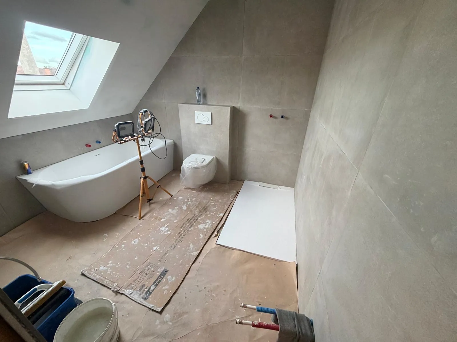 Vrijstaand bad, hangtoilet en douchebak geplaatst in een getegelde badkamer onder het dak, door HS Concept in Aalst