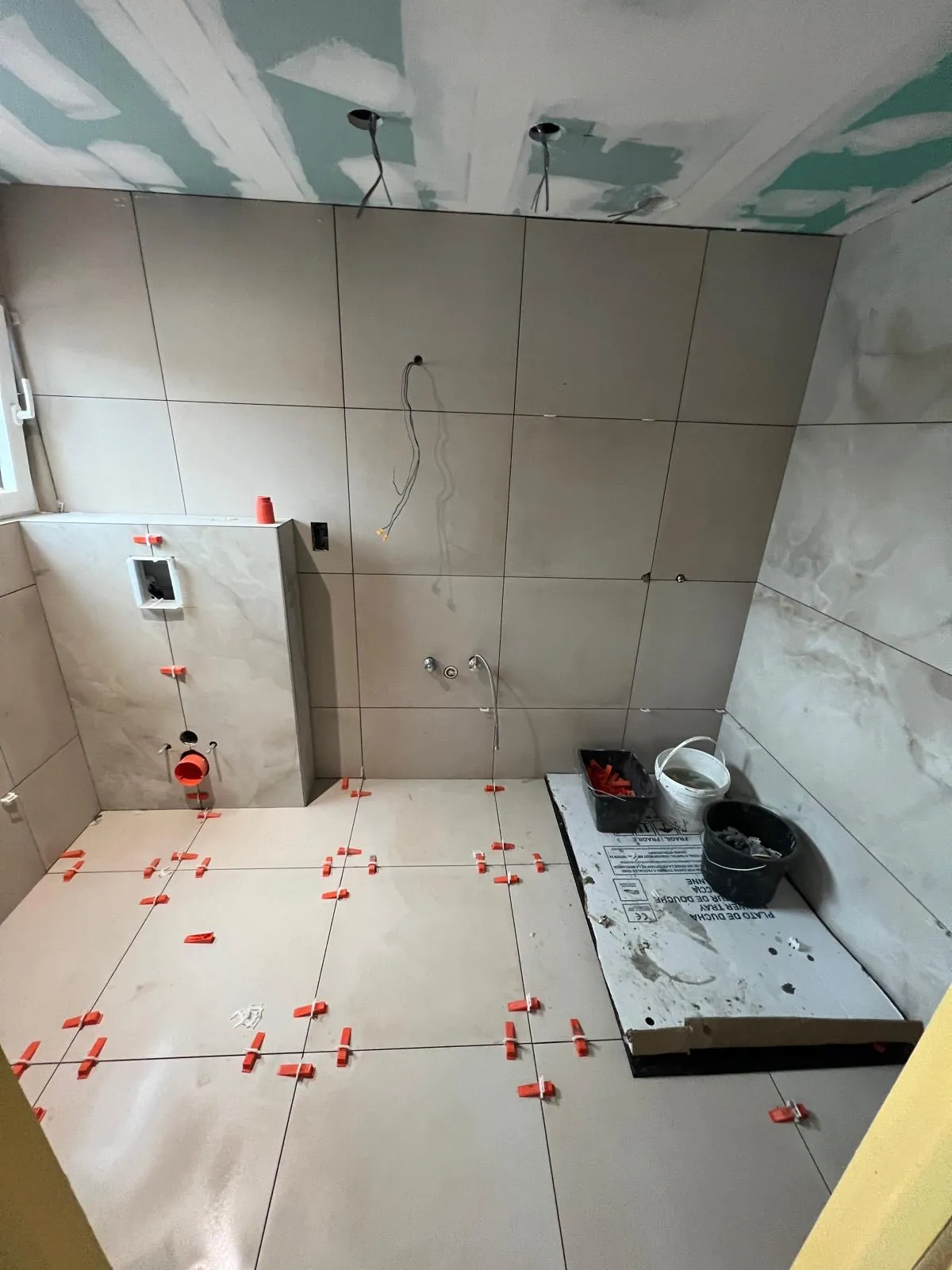 Tegelwerk in uitvoering in een badkamer met nivelleerclips en ingewerkte leidingen, werk van HS Concept in Aalst